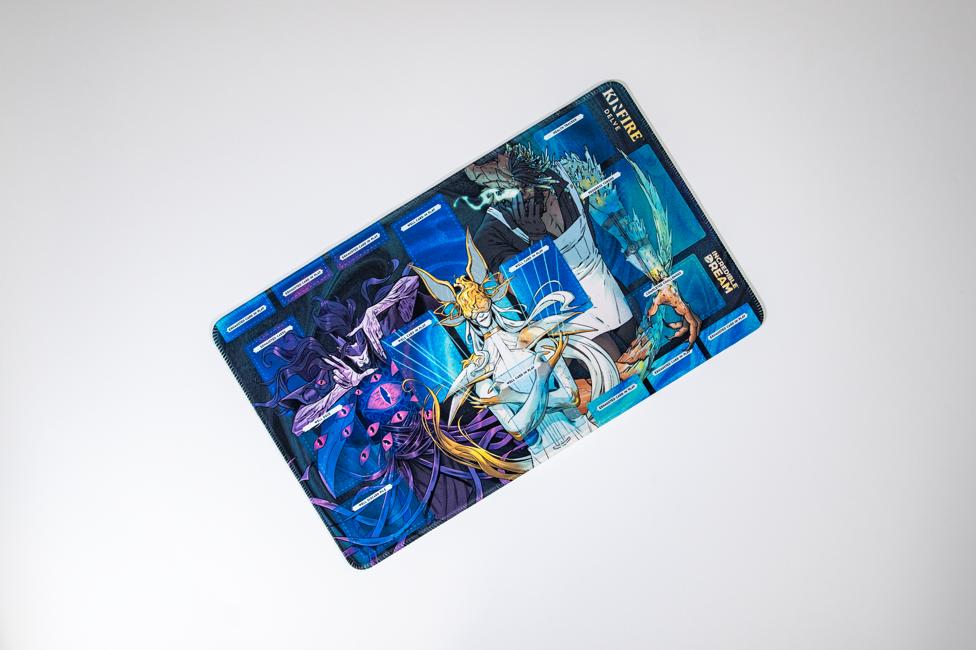 A vibrant Kinfire Delve game playmat displaying fantasy art of characters and labeled zones for cards