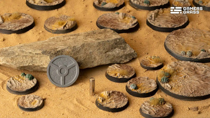 Desert-themed miniature bases with cacti and rocks, displayed on sand alongside magnet components and a large rock