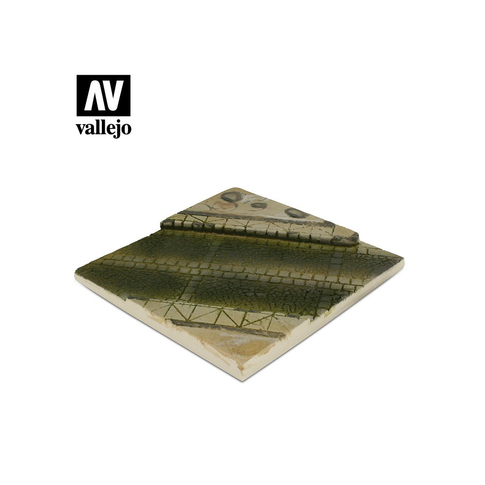 A Vallejo square miniature terrain base featuring a dark green, cracked path and an elevated lighter dirt section