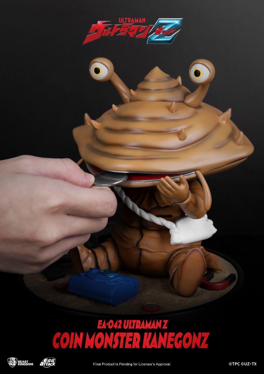 Hand inserting a coin into the open mouth of a Kanegon figure from Ultraman Z with a blue block and coins on the base