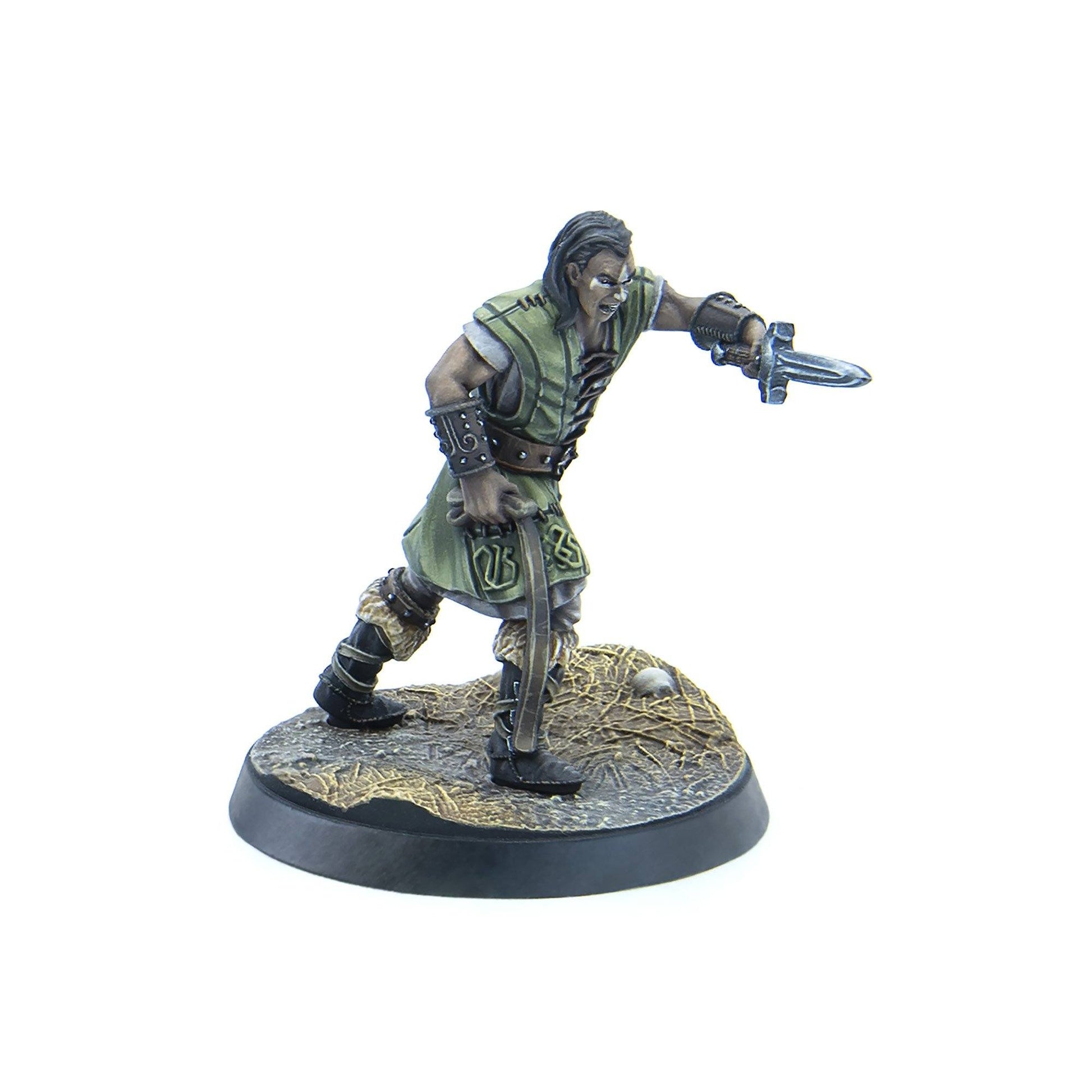 A grimacing male warrior miniature in green and leather armor lunges, wielding a dagger forward and a curved blade