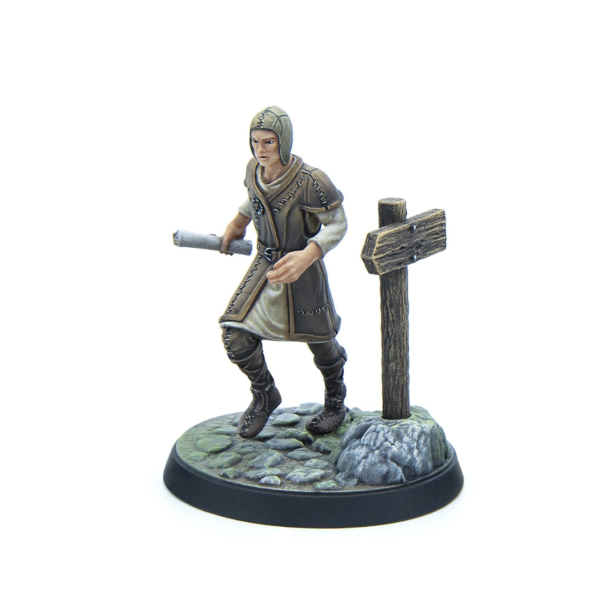 A painted miniature figure of a medieval-style person in a hooded cap and tunic, striding with a scroll past a wooden signpost