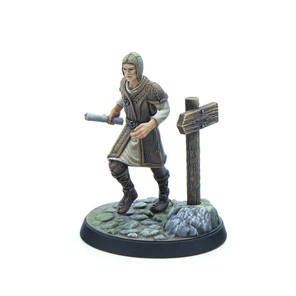 A painted miniature figure of a medieval-style person in a hooded cap and tunic, striding with a scroll past a wooden signpost