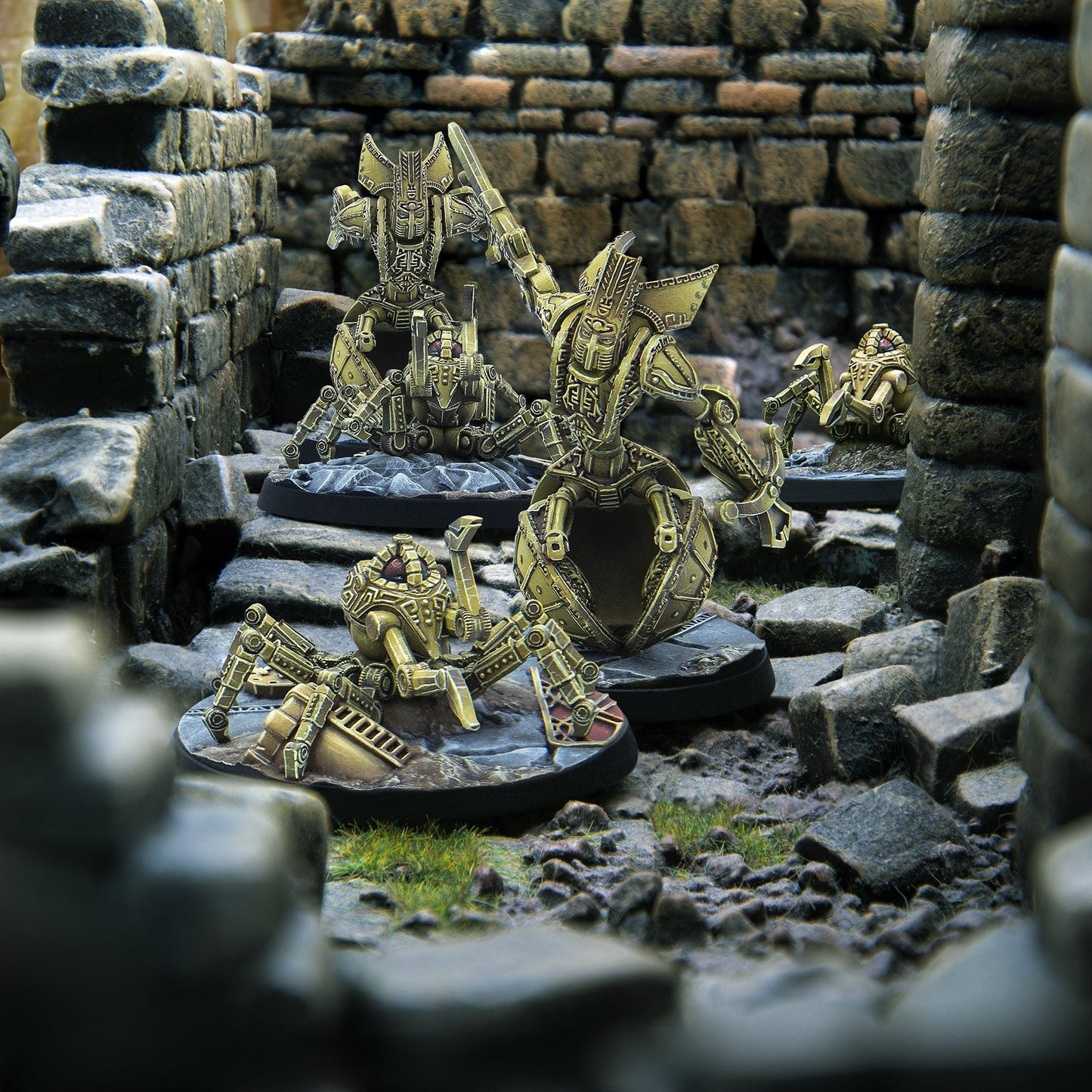 Golden robot and spider-like miniatures stand in stone ruins, one larger robot wielding a sword