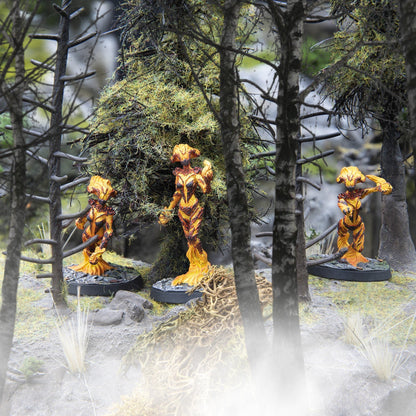 Three vibrant orange and yellow flame-like miniatures stand in a misty, moss-covered miniature forest