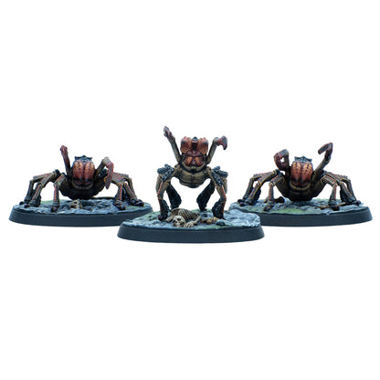 Three brown and red spider-like miniatures on bases, the central one rears up over a small skeleton