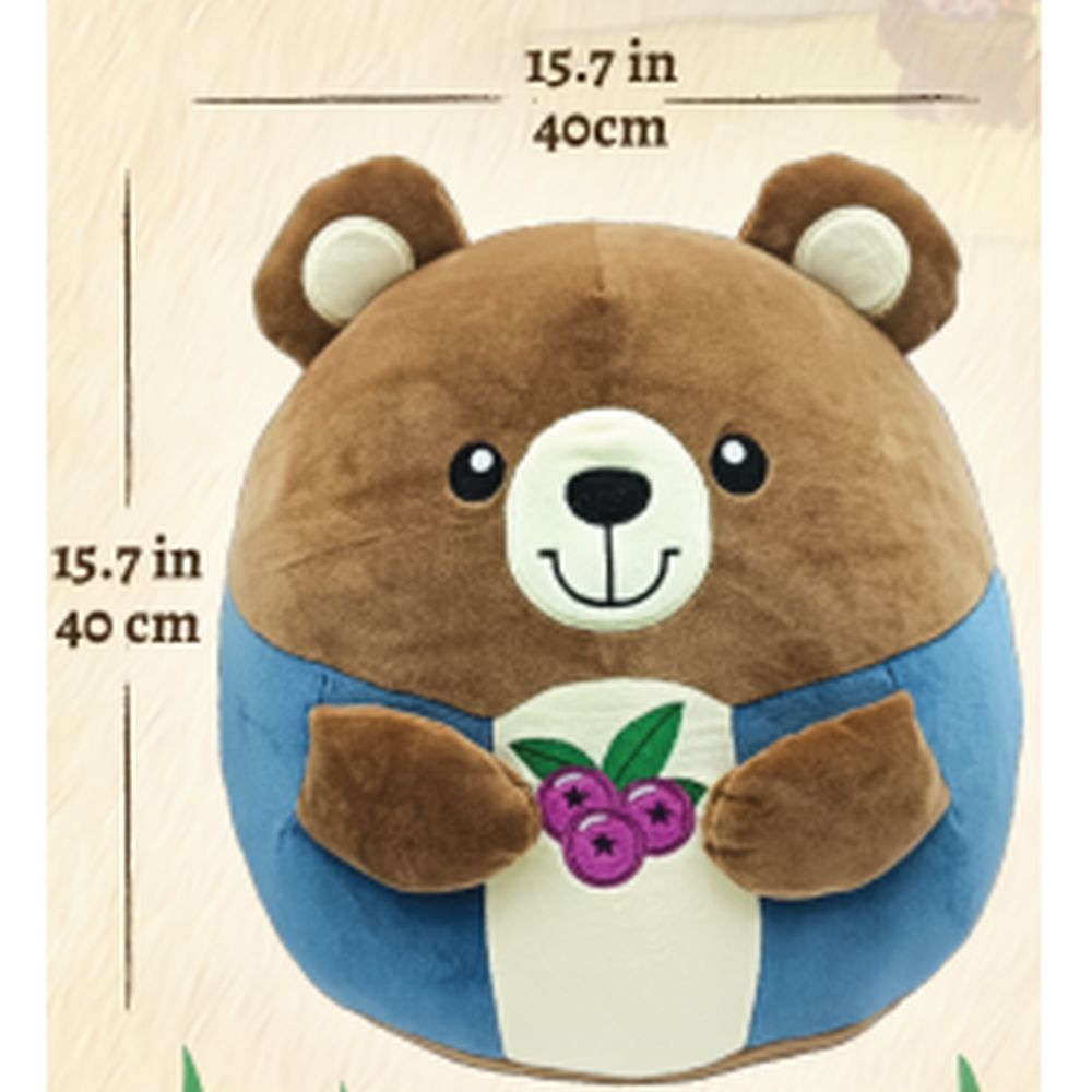 A smiling brown plush bear wearing blue overalls and a white belly, holding purple berries with green leaves.
