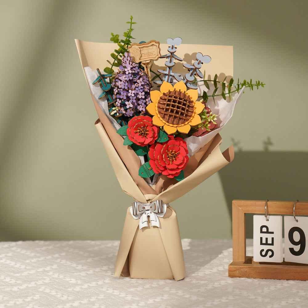 Colorful bouquet of laser-cut wooden flowers (sunflower, red, purple) wrapped in paper, next to a "SEP 9" calendar