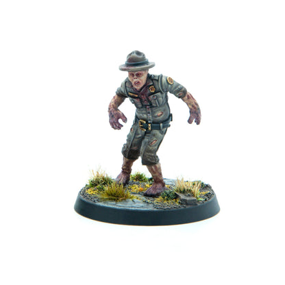 A miniature zombie park ranger in a tattered, bloody uniform, standing menacingly on a dirt and grass base