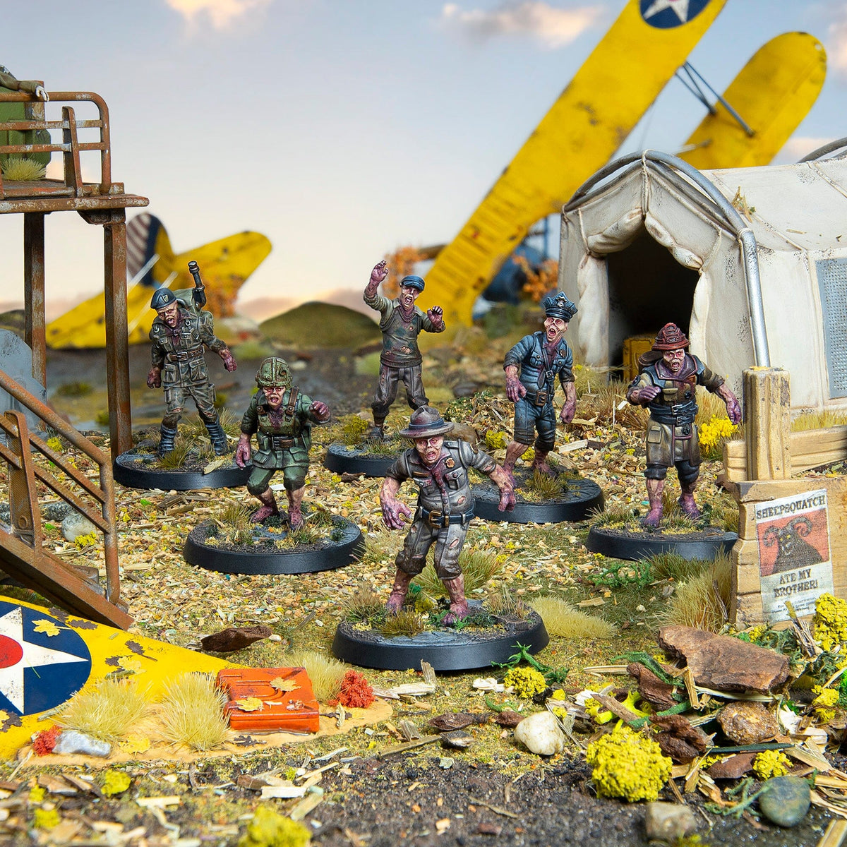 Six zombie miniatures in military and civilian uniforms shamble across a ruined airfield with a crashed yellow biplane and tent