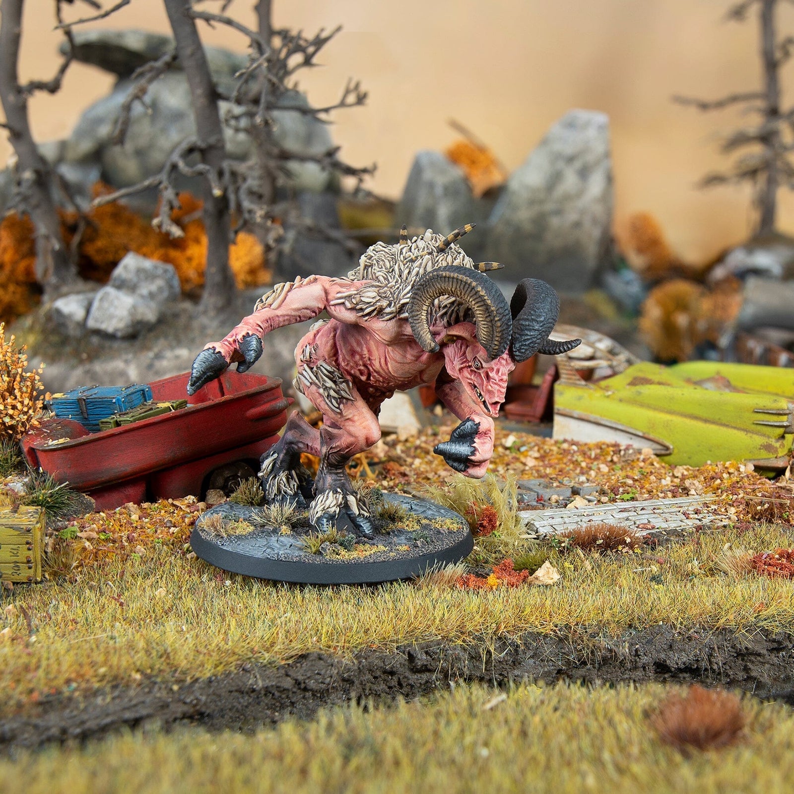 Miniature of a pink, ram-horned mutant charging in a detailed wasteland diorama with wreckage