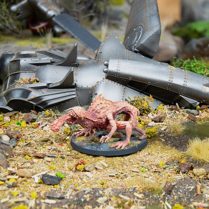 Fleshy, pink monster miniature stands on a diorama base next to large metallic wreckage