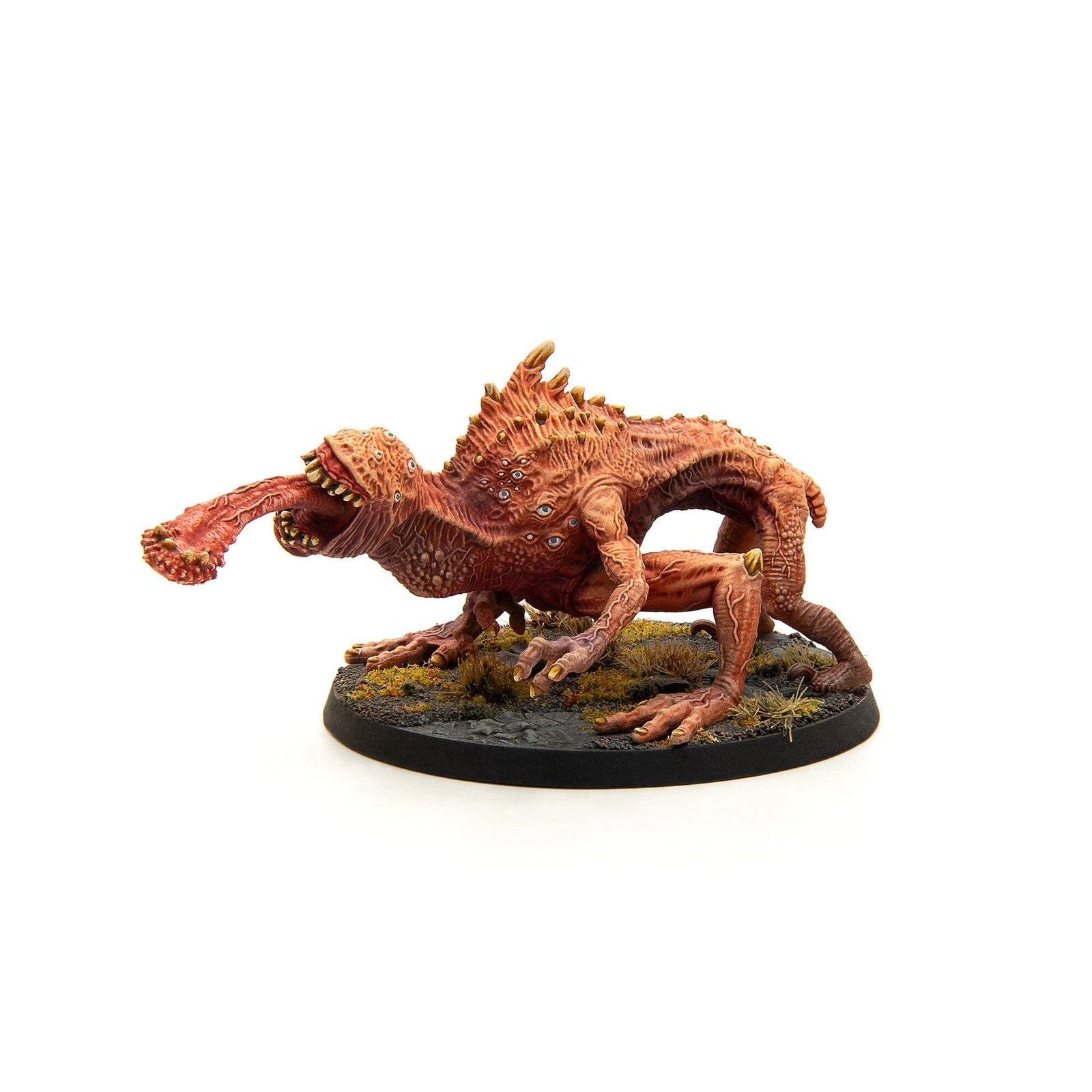 Spiky, multi-eyed red miniature creature lunging forward with a thick, club-tipped tongue on a terrain base
