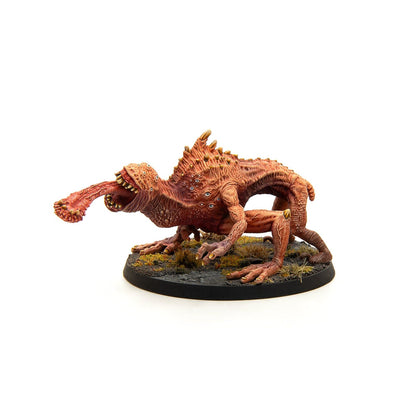 Spiky, multi-eyed red miniature creature lunging forward with a thick, club-tipped tongue on a terrain base