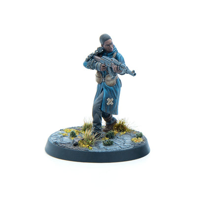 A painted miniature of a dark-skinned figure in a blue coat, ammo bandolier, holding an assault rifle, striding on a textured base.