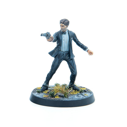 A painted miniature figure of a man in a dark suit and bow tie, aiming a pistol forward.