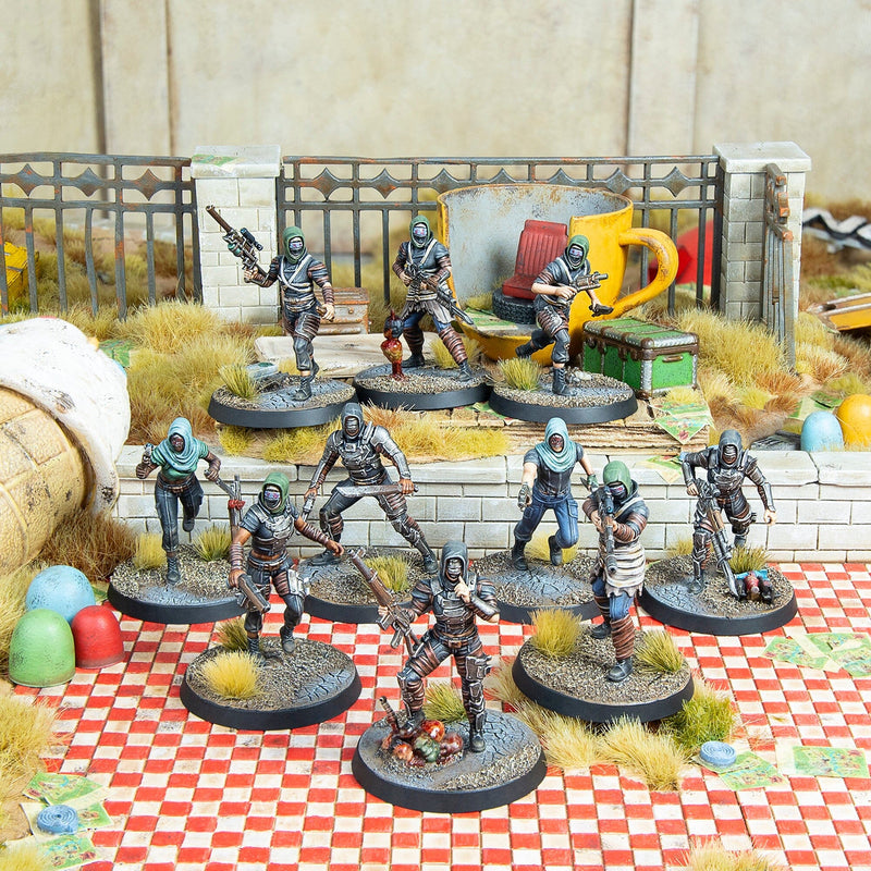 Ten hooded, armed miniature figures on a diorama with a giant yellow mug, a fence and checkered ground