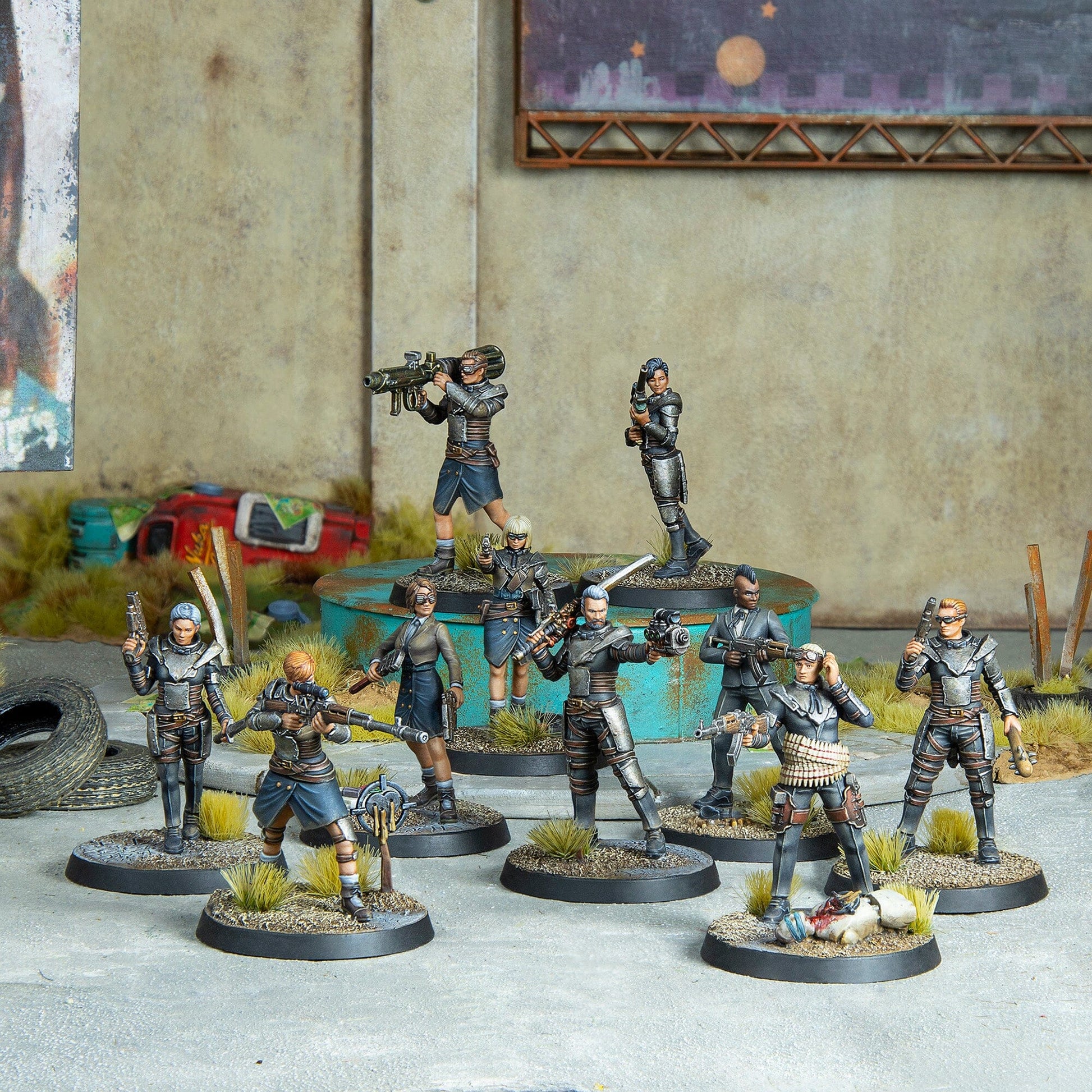 Ten armed post-apocalyptic miniature figures stand in a ruined setting; one figure is posed over a fallen enemy