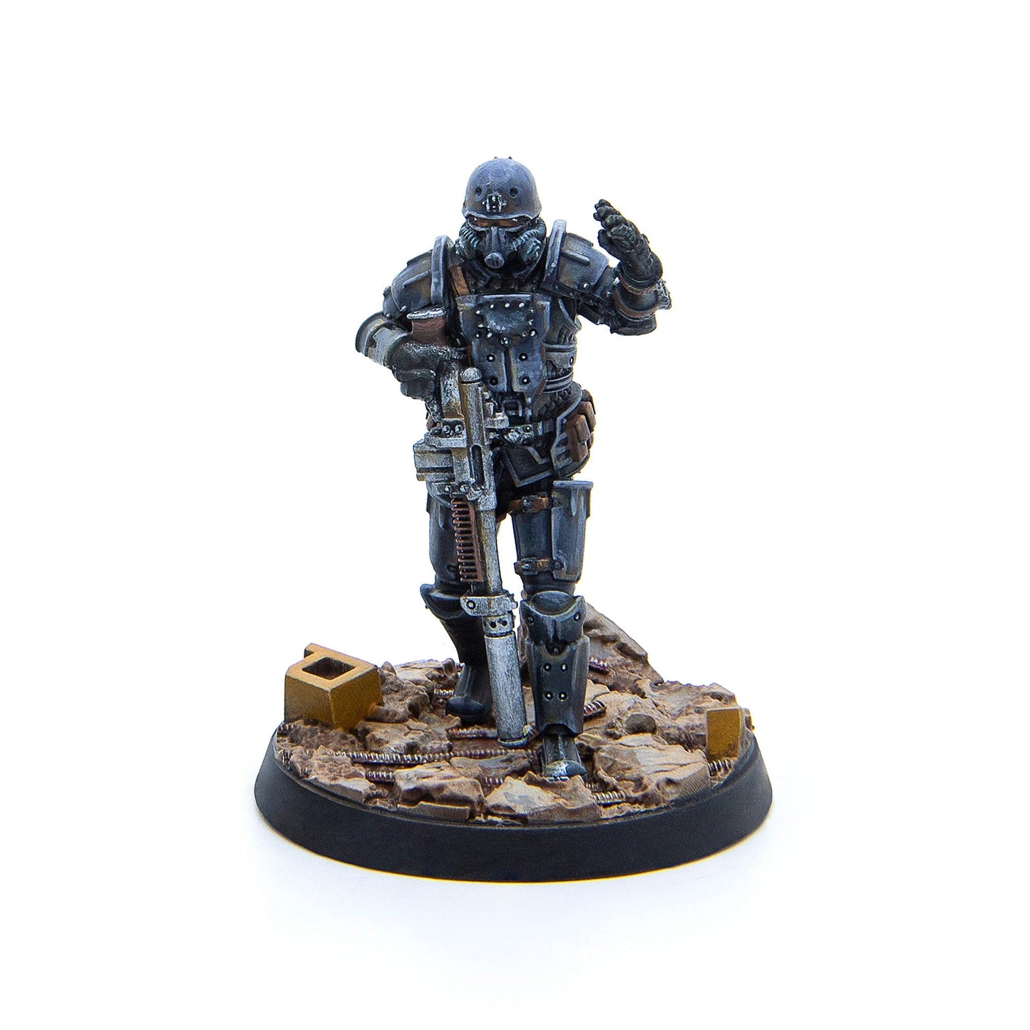 A painted miniature figure of a soldier in dark armor, helmet, and gas mask holds a rifle and gestures with a raised hand, standing on a textured base with debris