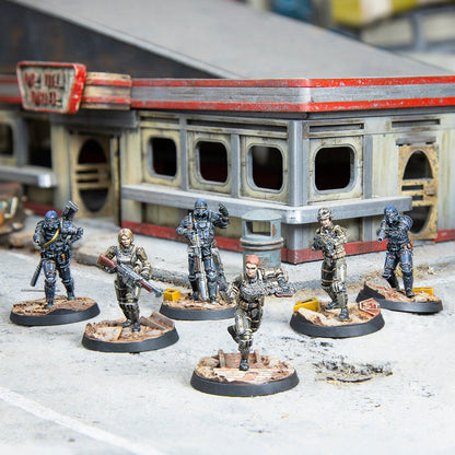 Six miniature figures from Fallout Wasteland Warfare - Brotherhood of Steel Combat Patrol stand on a concrete surface in front of a weathered building