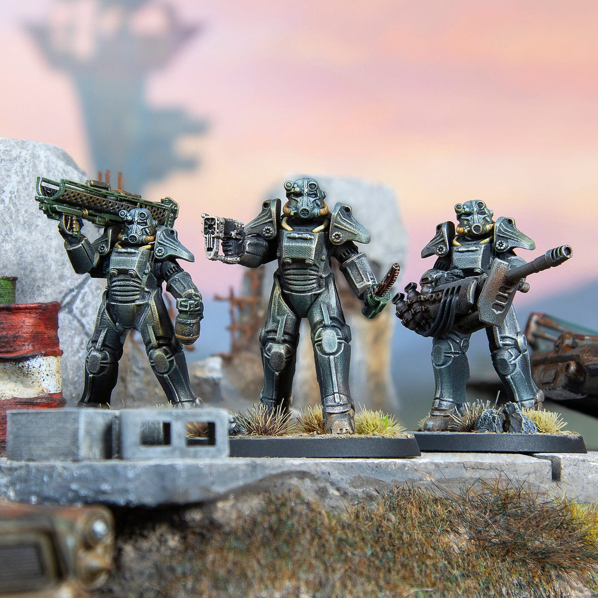 Three detailed Fallout The Roleplaying Game miniature figures in power armor, holding various weapons on a textured diorama base