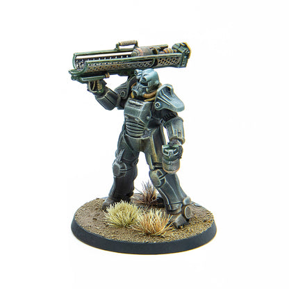 A Fallout Wasteland Warfare miniature depicts a Brotherhood of Steel figure in power armor holding a large rifle on a textured dirt base with dried grass