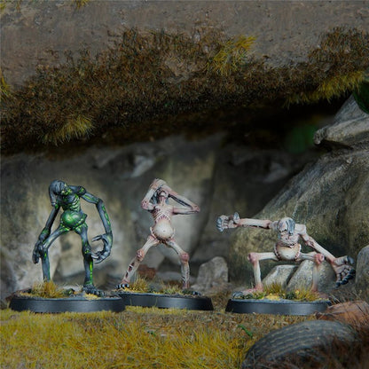 Three painted miniatures of gaunt, monstrous creatures: one green, one pale with hands over head, and one pale lunging, on rocky terrain.