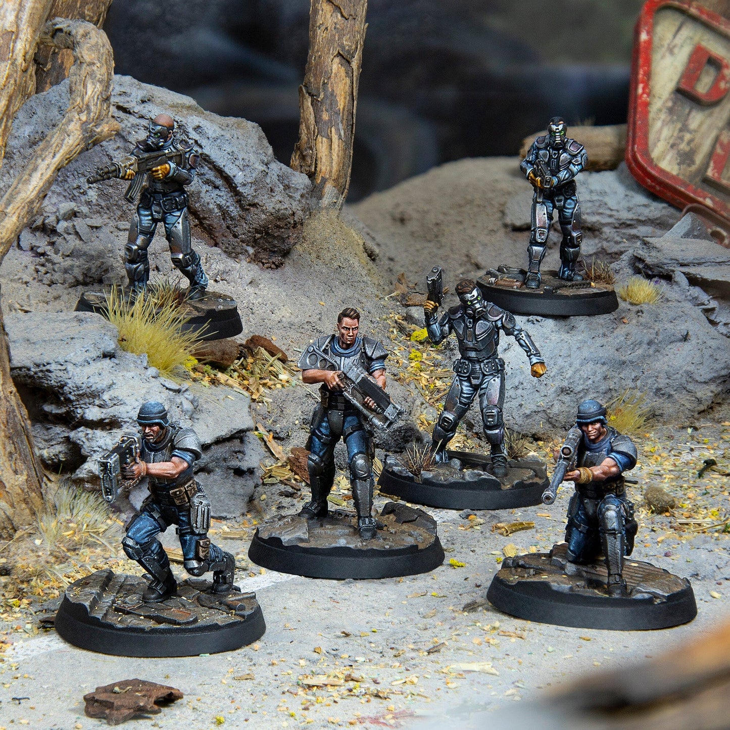 Six miniature armored soldiers stand ready with weapons on a detailed rocky, post-apocalyptic diorama