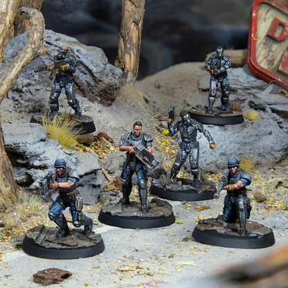Six miniature armored soldiers stand ready with weapons on a detailed rocky, post-apocalyptic diorama