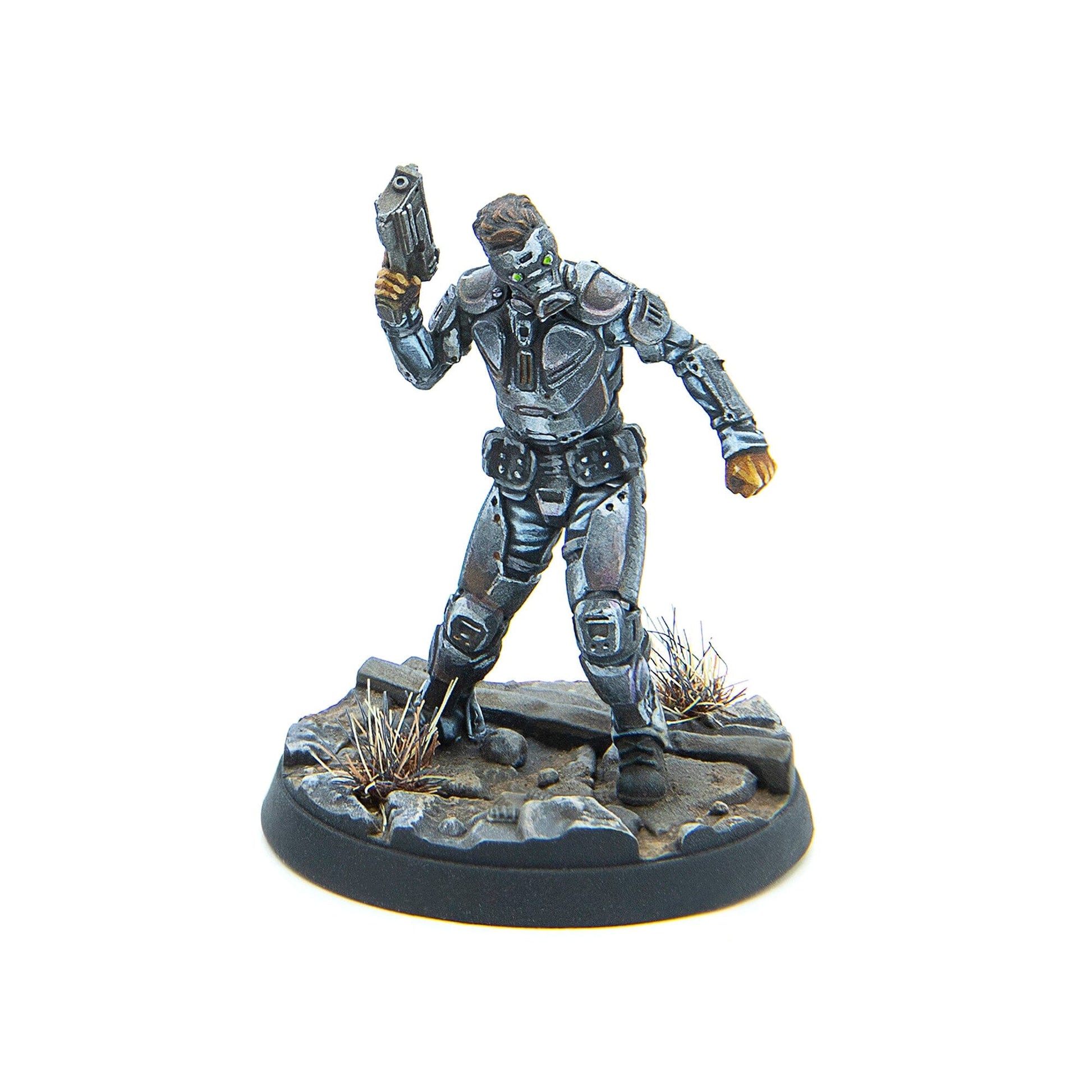 A silver-armored sci-fi miniature with green glowing eyes holds a pistol up, standing on a rocky, grassy base