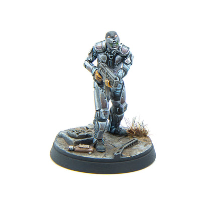 A miniature armored sci-fi trooper with a green glowing visor, holding a rifle, on a debris-strewn base