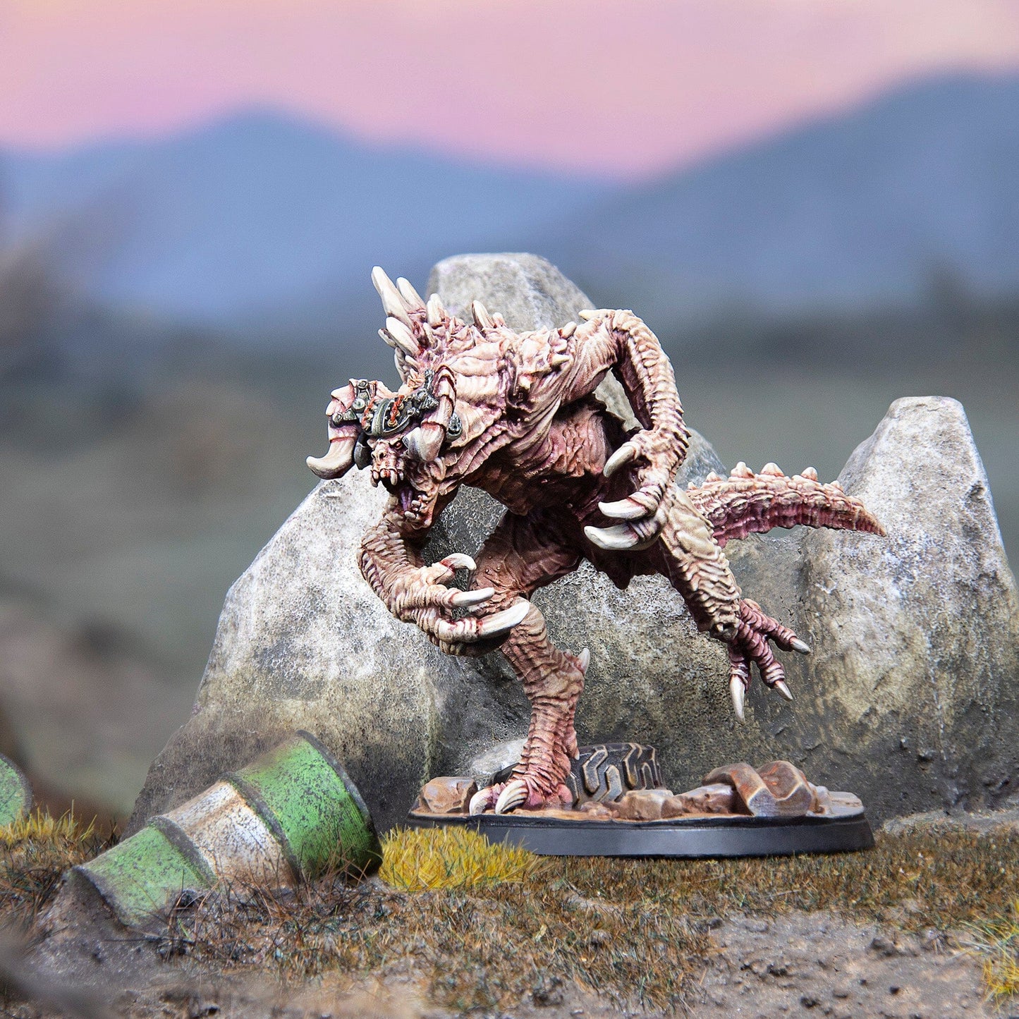 A detailed miniature of a beige bipedal monster with large claws and spikes stands on a rocky base in a barren landscape under a pink and blue sky