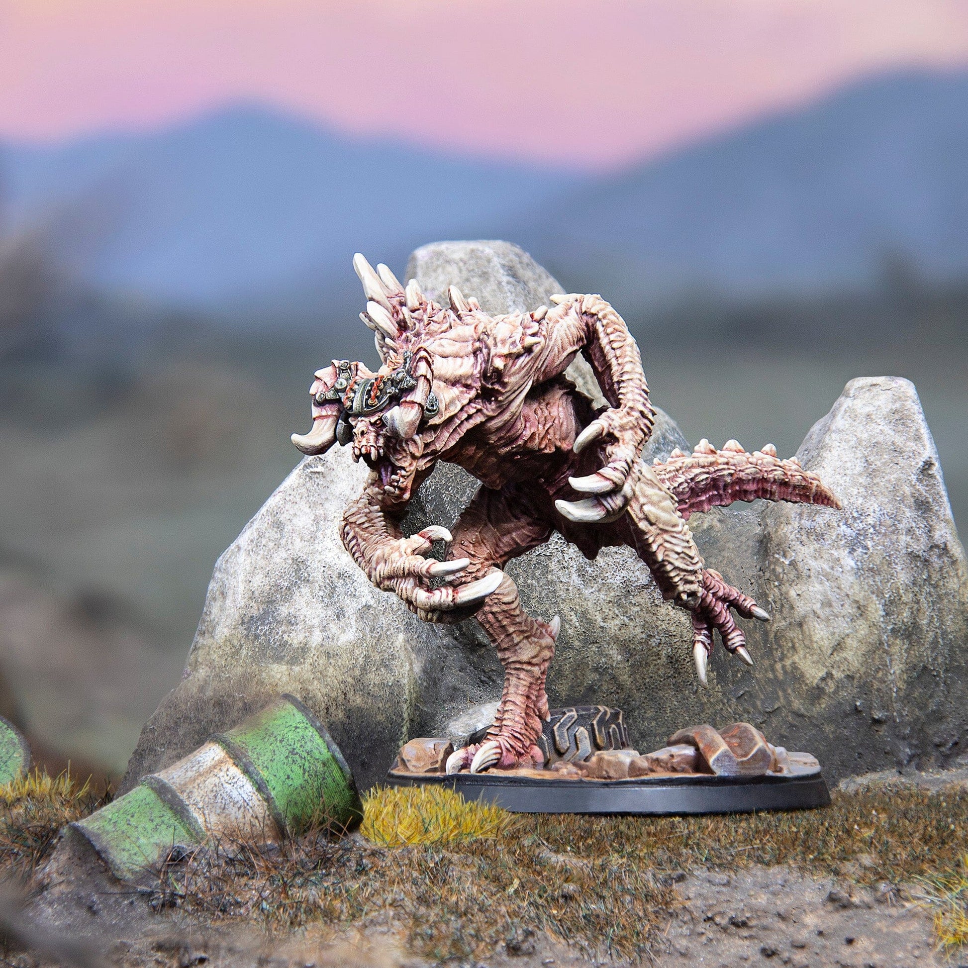 A detailed miniature of a beige bipedal monster with large claws and spikes stands on a rocky base in a barren landscape under a pink and blue sky