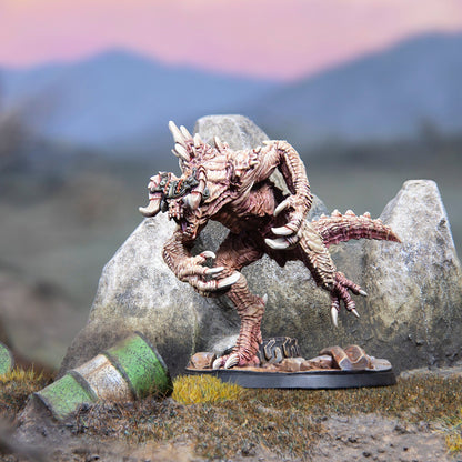 A detailed miniature of a beige bipedal monster with large claws and spikes stands on a rocky base in a barren landscape under a pink and blue sky