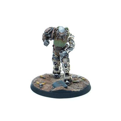 A miniature armored figure in green and brown armor with a helmet and face cage, stepping forward on a debris-strewn wasteland base