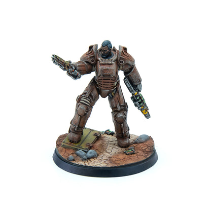 A miniature of a man in rusty Fallout power armor, holding a chainsaw weapon and energy rifle on a debris-strewn base