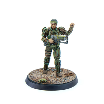 Green armored sci-fi miniature figure holding a rifle, with their left fist raised