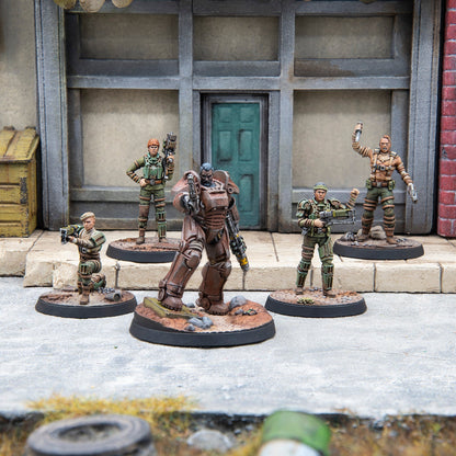 Five detailed post-apocalyptic miniatures, led by a power-armored figure, stand armed in a ruined city