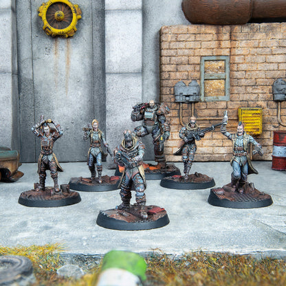 Six armed, post-apocalyptic miniature figures in dynamic poses stand on a concrete ground in a dilapidated urban scene