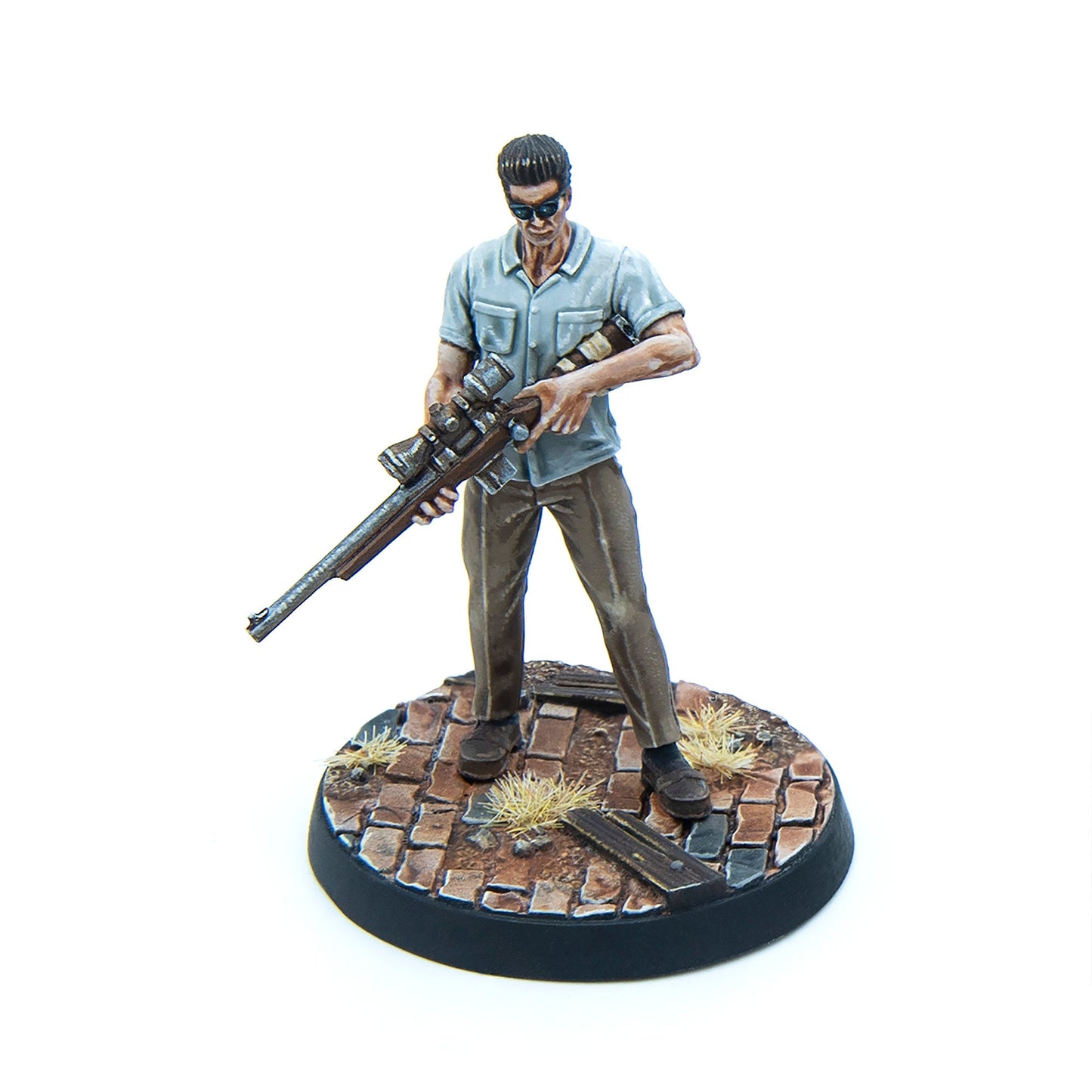 Painted miniature of a smirking man in sunglasses, holding a sniper rifle across his body, on a cobblestone base