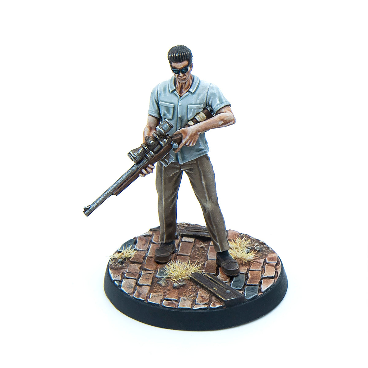 Painted miniature of a smirking man in sunglasses, holding a sniper rifle across his body, on a cobblestone base