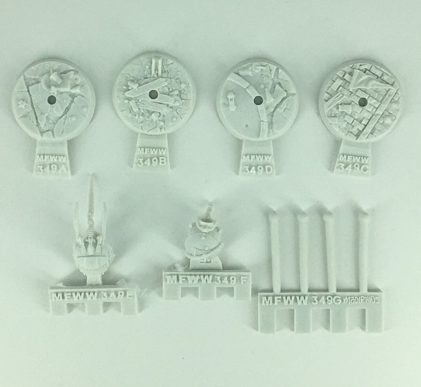 Unpainted light grey model kit parts: four textured bases, two detailed mechanical pieces, and four cylindrical rods