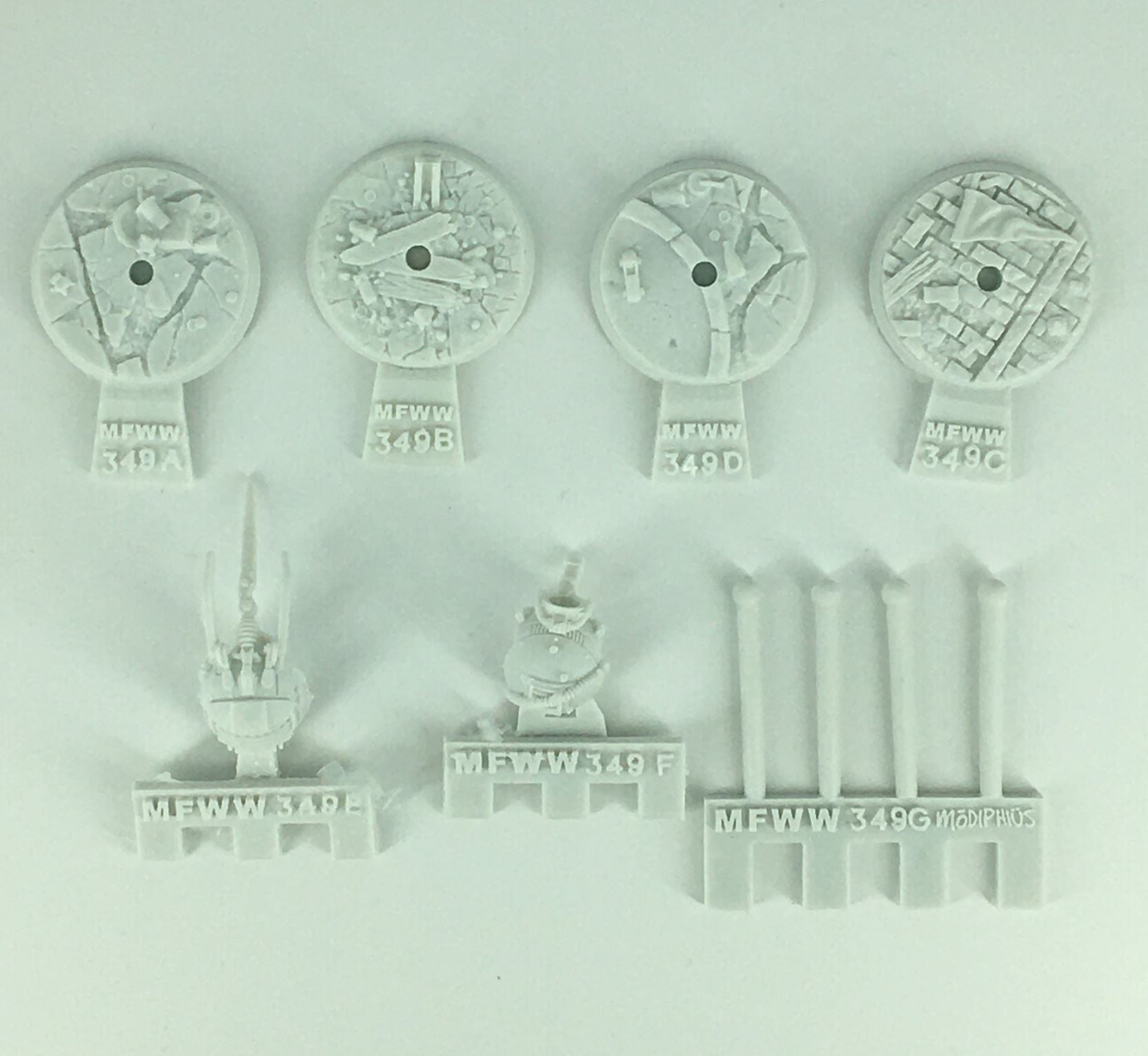 Unpainted light grey model kit parts: four textured bases, two detailed mechanical pieces, and four cylindrical rods