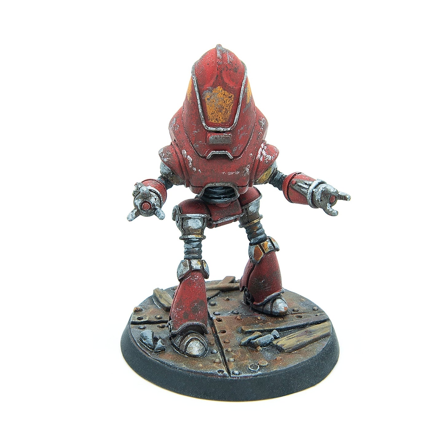 A weathered, rusty red robot miniature crouches with arms extended on a metal plate base