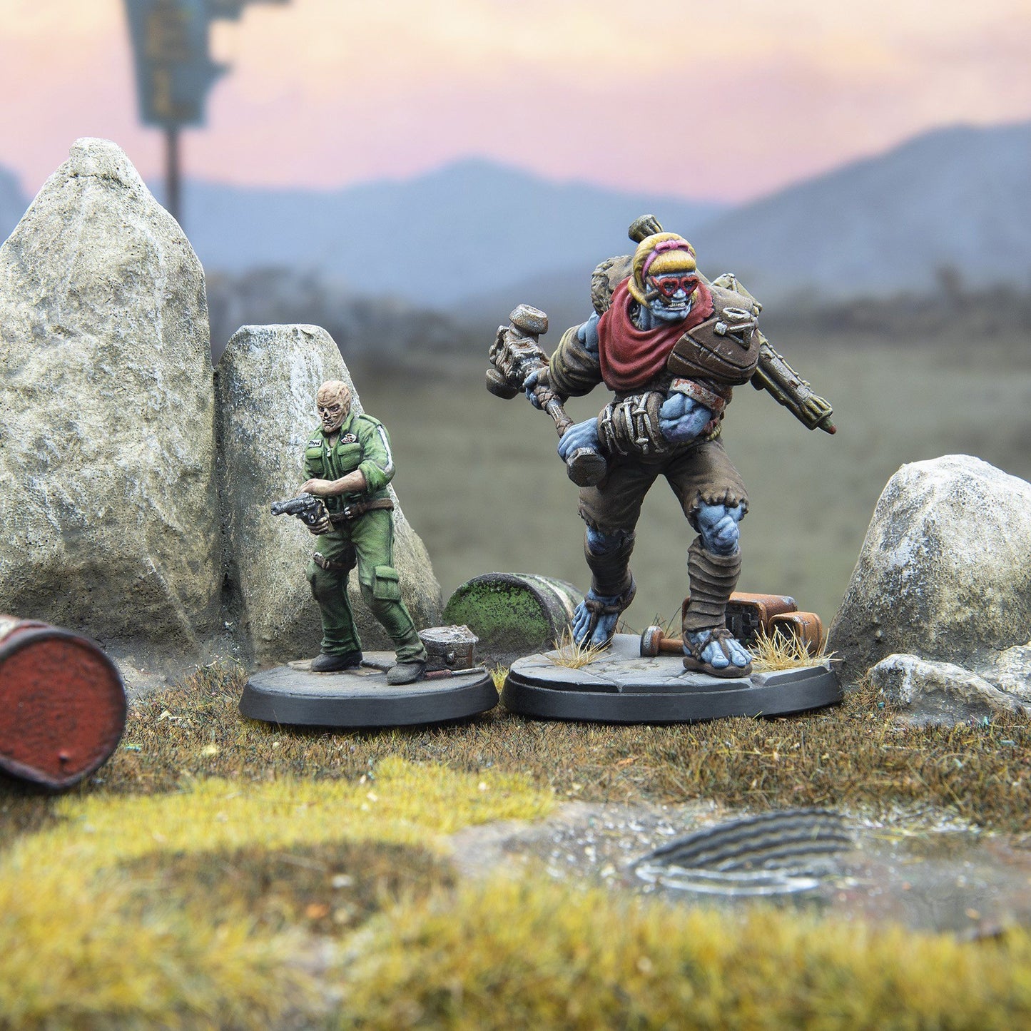 Two painted miniatures: a man holding a pistol and a large blue mutant with heart sunglasses and a hammer, in a rocky wasteland