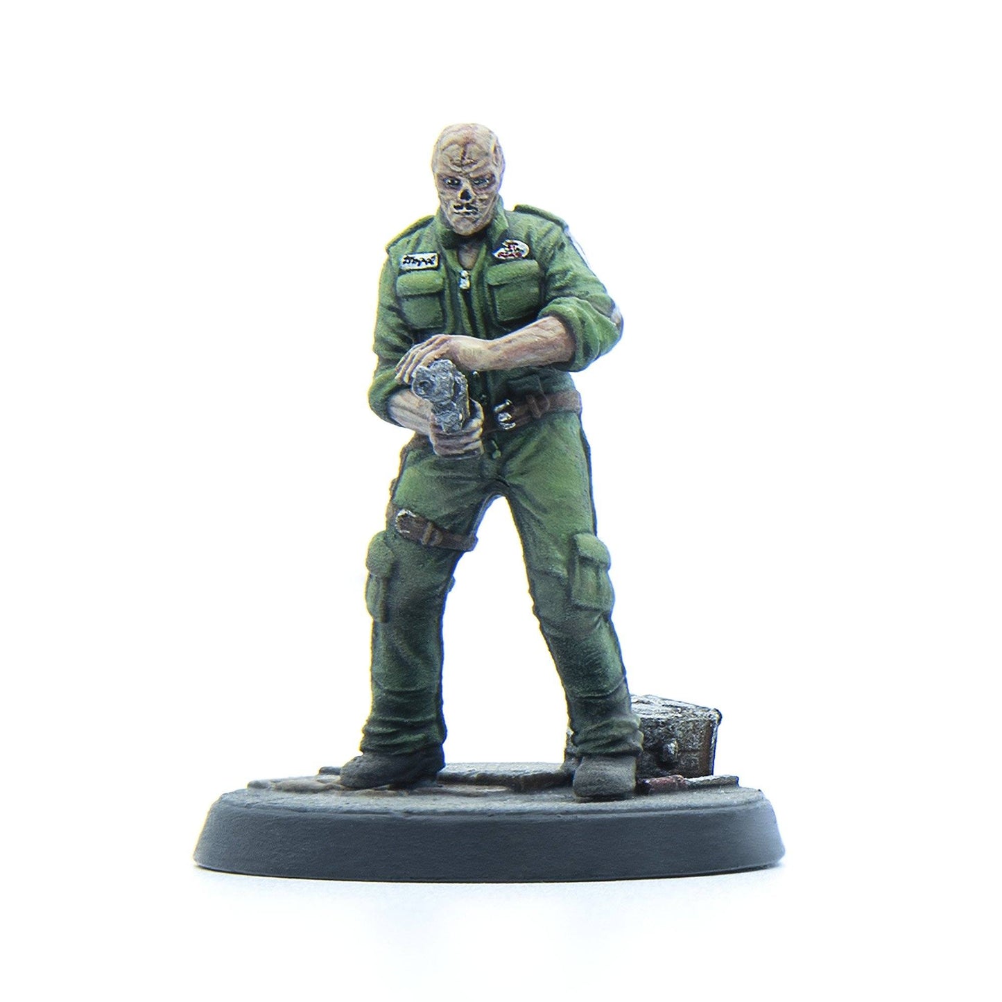 A miniature of a pale, bandaged-faced figure in green fatigues holding a pistol, standing on a round base