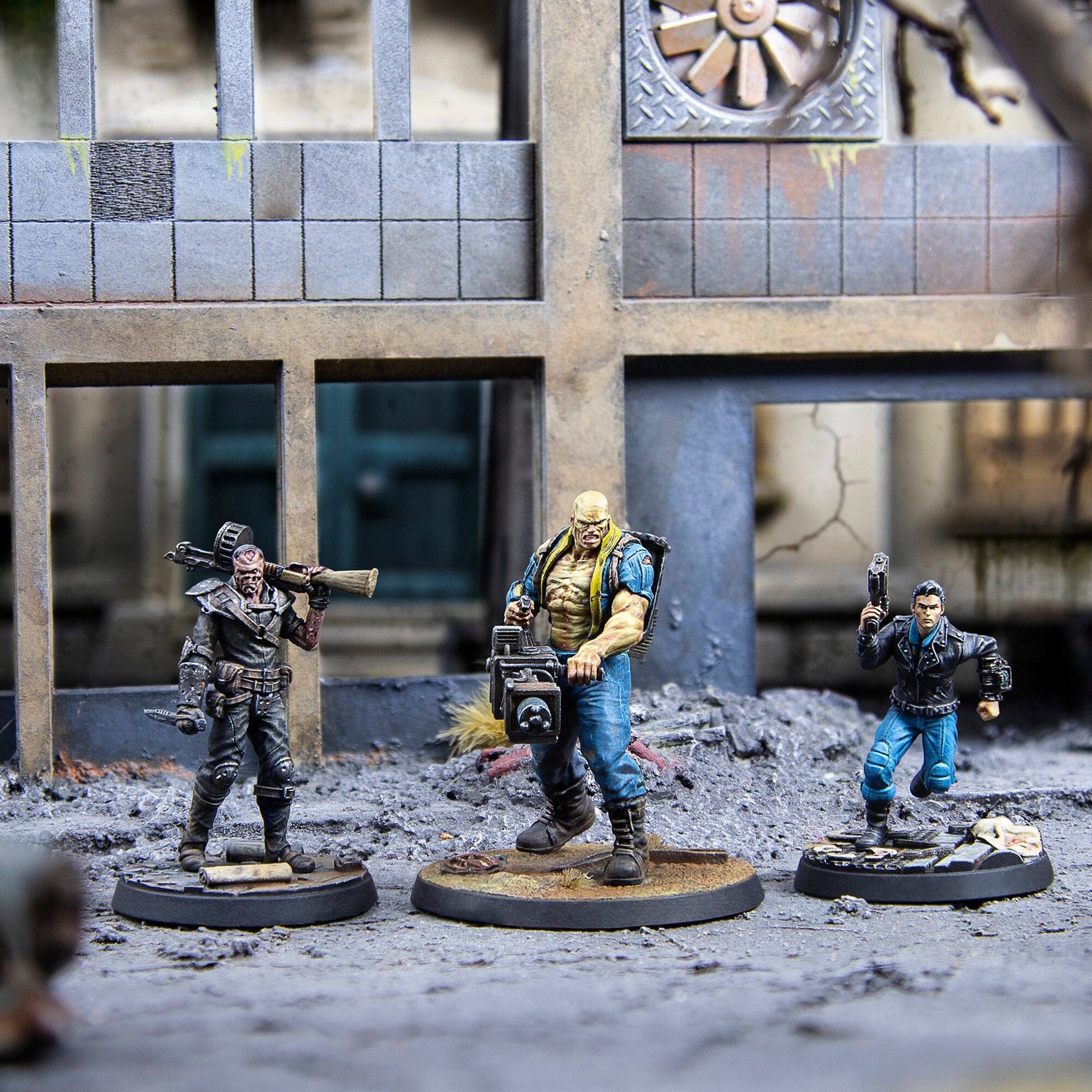 Three detailed miniature post-apocalyptic warriors with a rocket launcher, heavy gun, and pistol stand on rubble