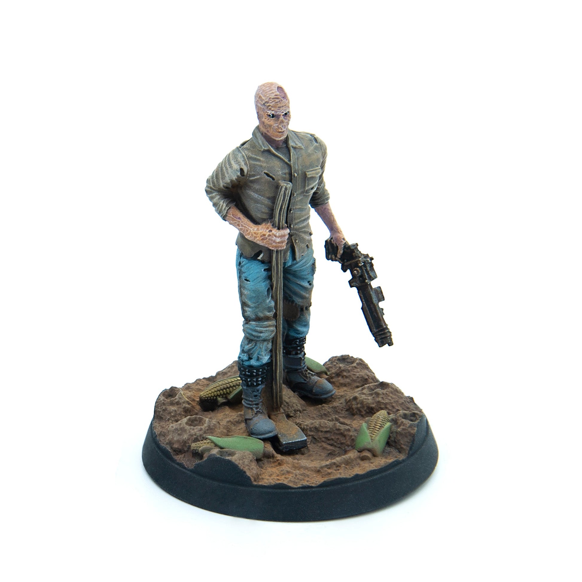 A miniature of a mutated man in worn clothes, holding a staff and a gun, on an earthy base with scattered corn