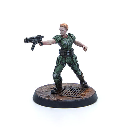 A miniature female soldier in green armor with short blonde hair aims a futuristic submachine gun on a dirty base with a grate