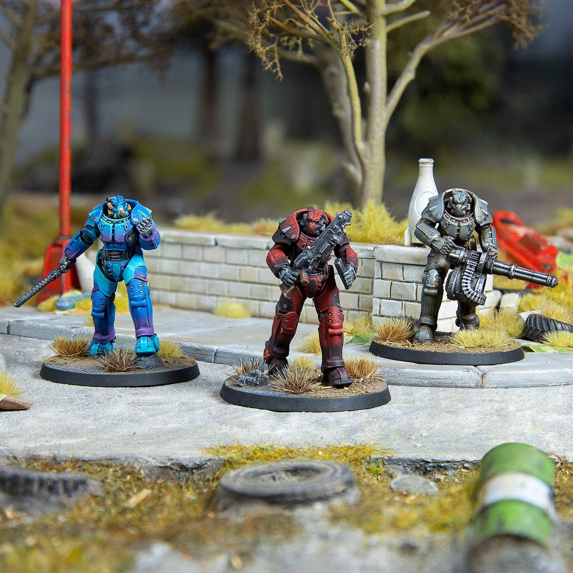 Three power-armored soldier miniatures: blue with blade, red with rifle, grey with minigun, on an urban diorama